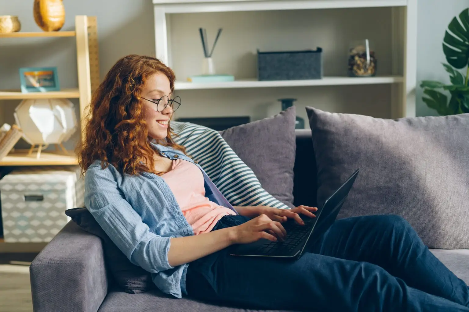 woman on couch smiling using laptop